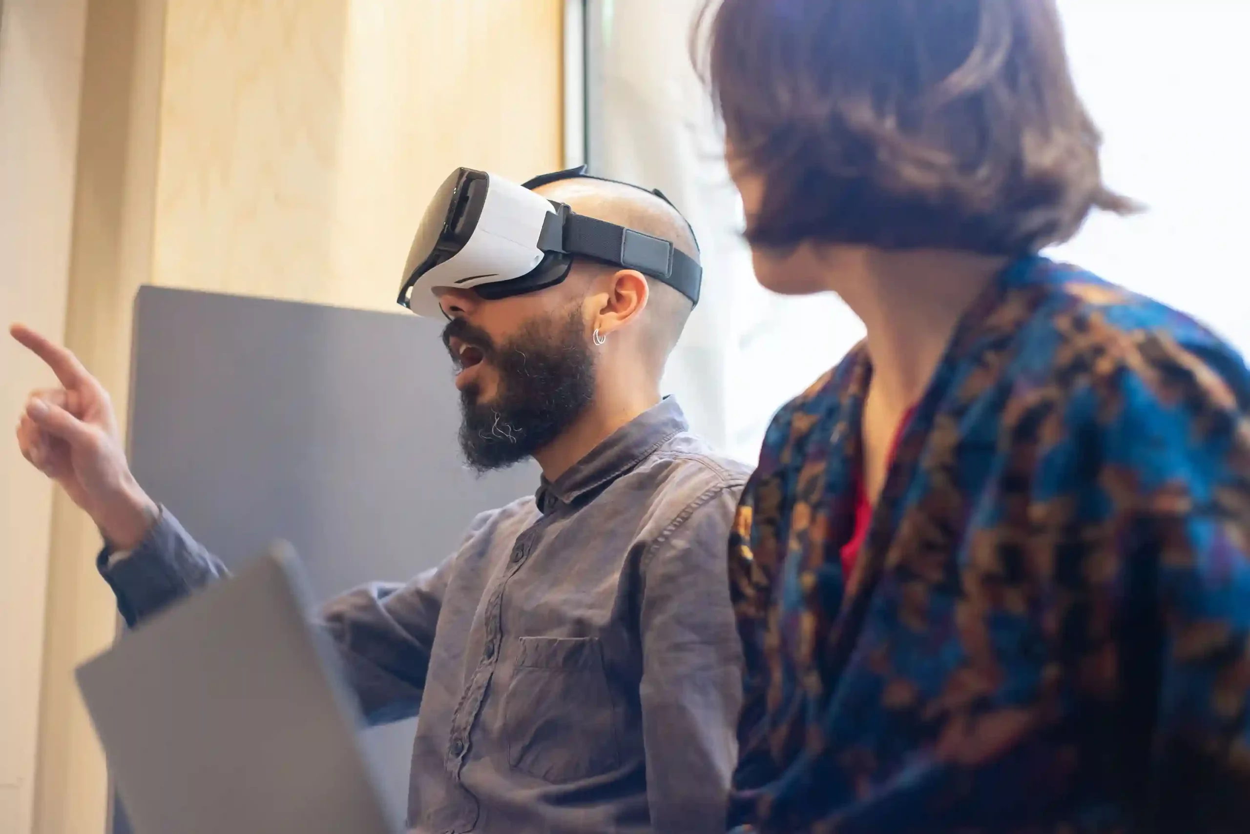 Client explorant un environnement virtuel depuis un bureau et échangeant avec une professionnelle de l’immobilier